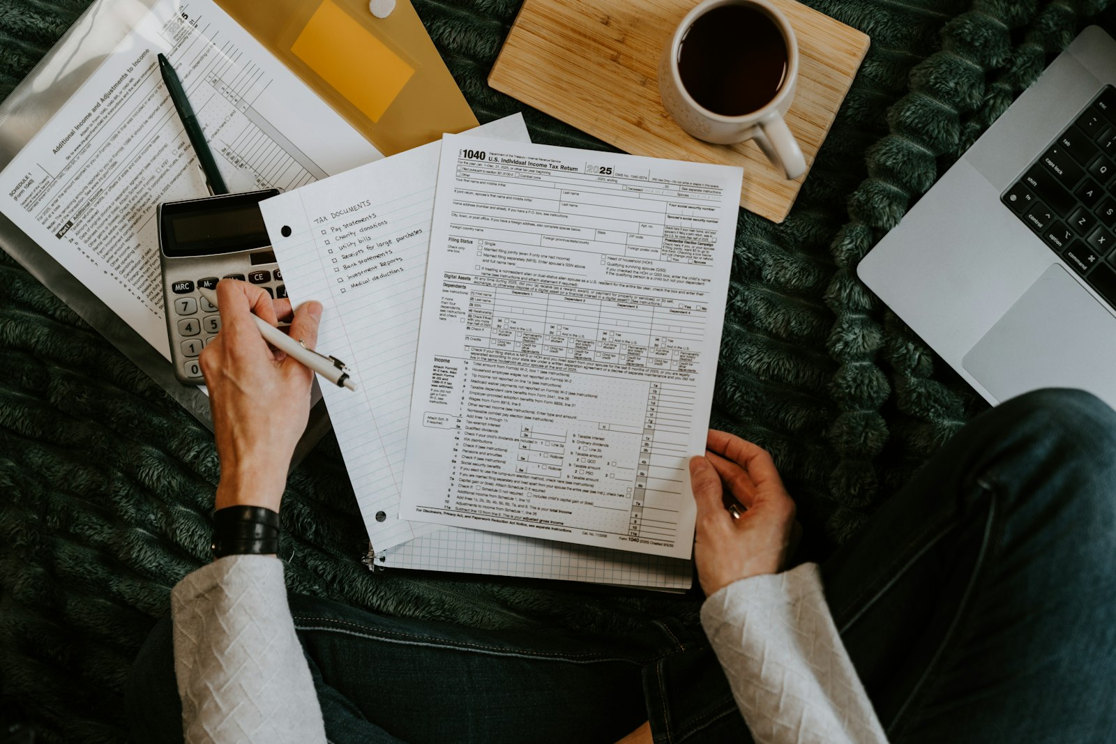 Person reviewing paper documents with a calculator and laptop to check the accounts