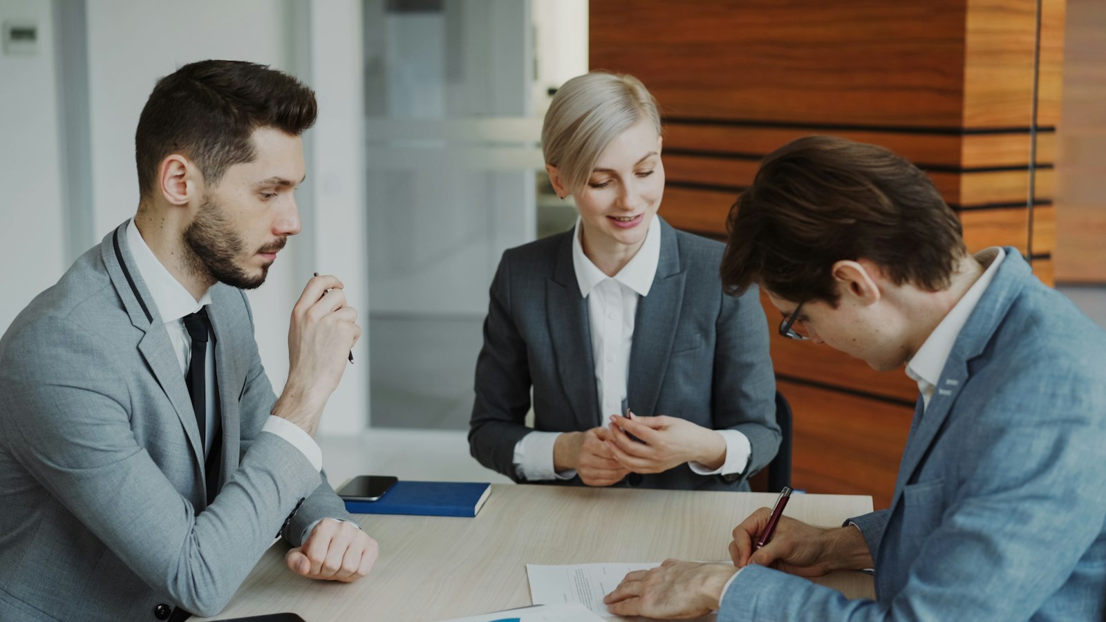 Business people signing a contract at a table while a lawyer explains the details