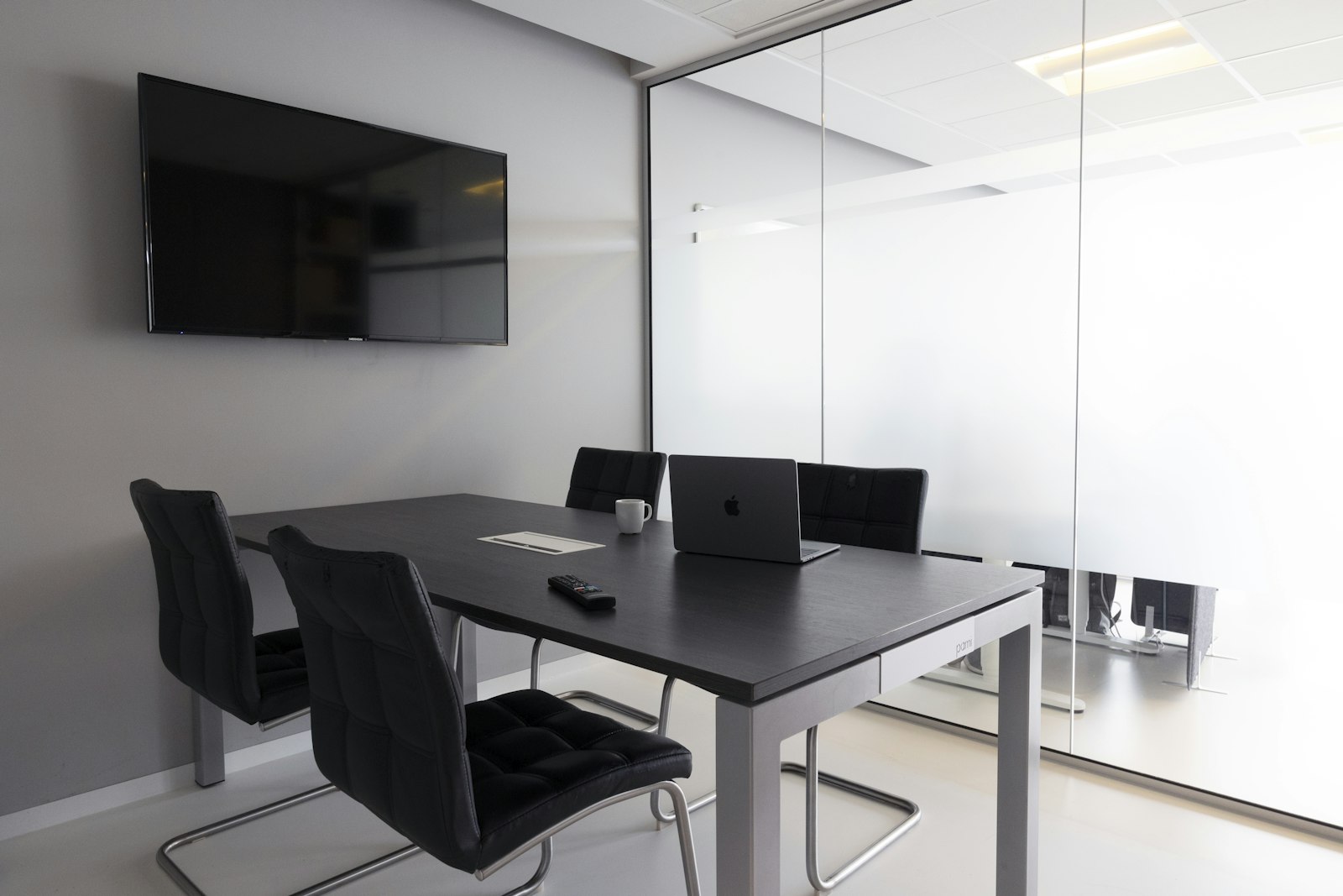 Small empty meeting room with a table, chairs, a wall-mounted television screen and a laptop