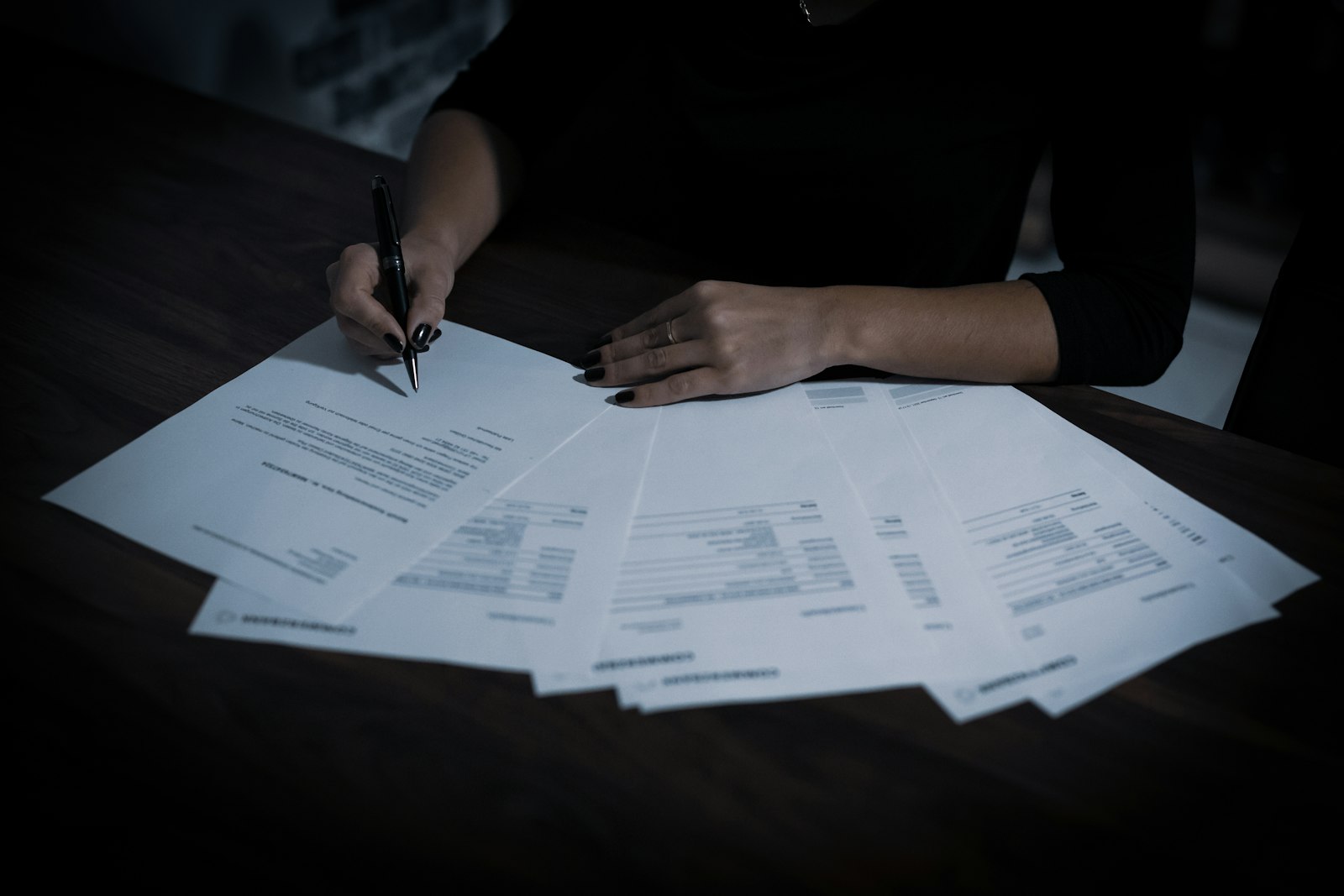 Woman signing a document with a ballpoint pen at a table covered in papers